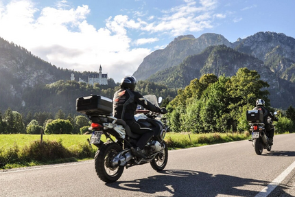 MoHo Schönauer Hof- Tour 7 Kulturtour Zwei Motorradfahrer fahren auf einer Bergstraße mit Schloss und Bergen im Hintergrund