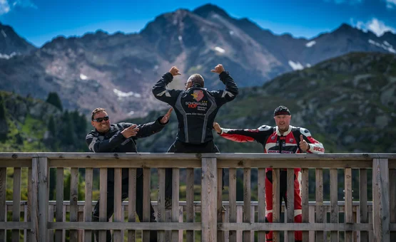 Drei Motorradfahrer posieren vor Berglandschaft auf einer Holzplattform