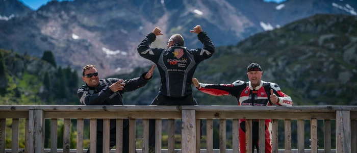 Three motorcyclists posing on wooden platform with mountain background