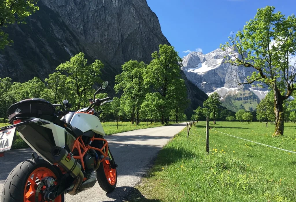Motorrad auf Landstraße mit Bergen und Bäumen im Hintergrund