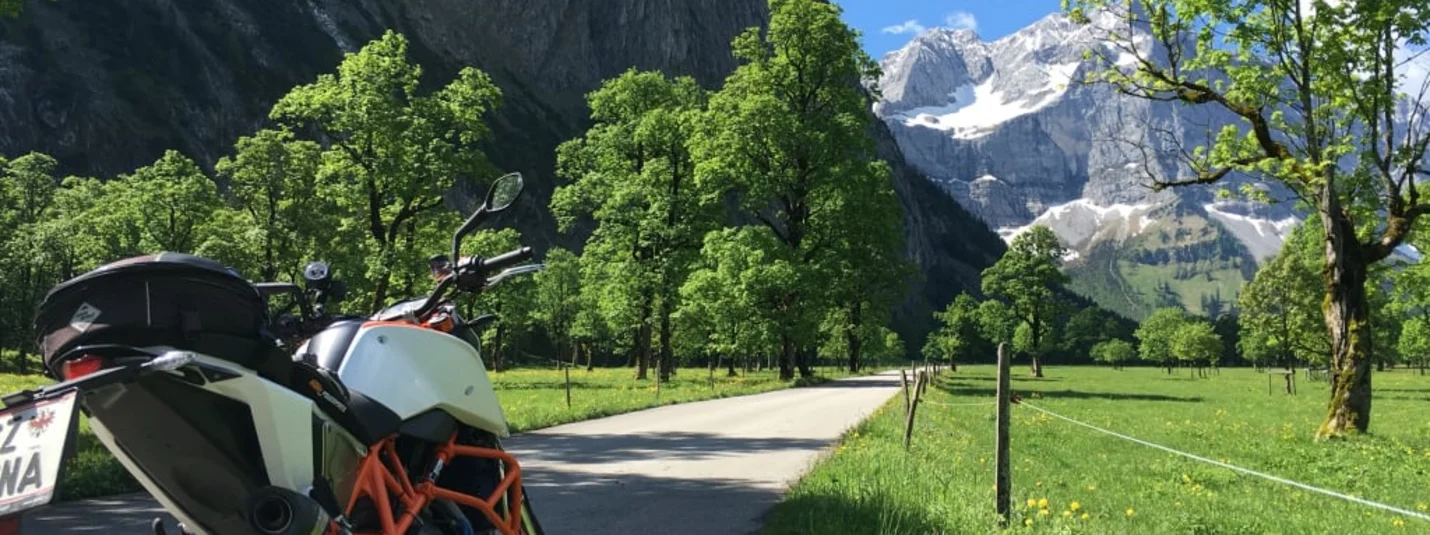 Motorrad auf Landstraße mit Bergen und Bäumen im Hintergrund