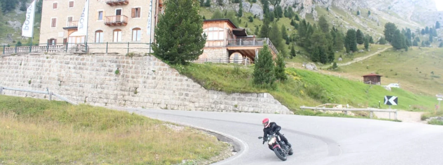 Motorcycle rider on winding mountain road near Hotel Pordoi and rocky cliffs