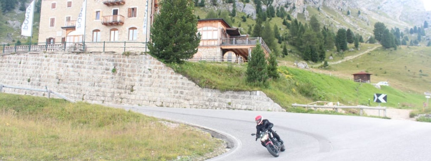 Dolomites Motorcycle Holiday – Hotel Jonathan Motorcycle rider on winding mountain road near Hotel Pordoi and rocky cliffs