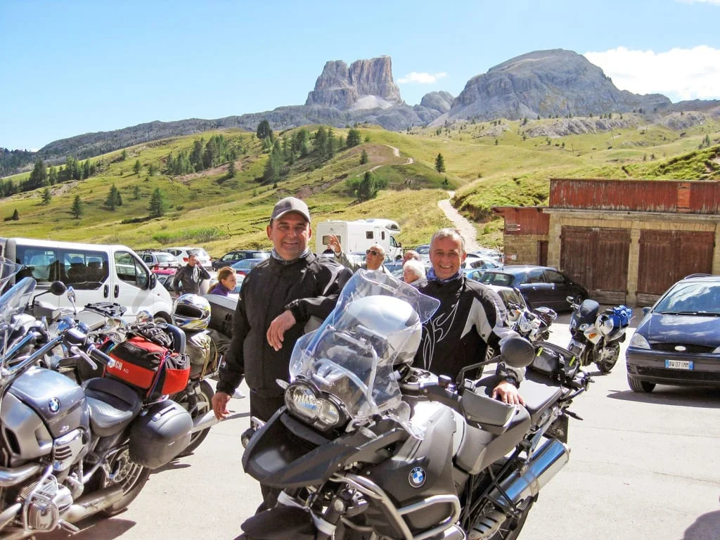 Two men with motorcycles in front of mountain landscape on sunny day