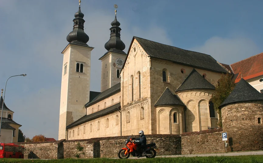 Person riding motorcycle in front of monastery church with twin towers under clear sky
