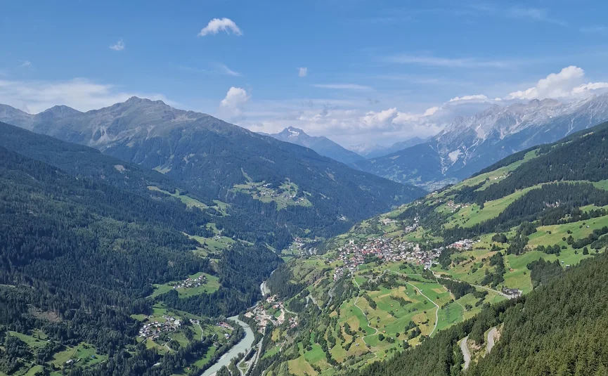 View of a green valley with river, forest, and mountains under blue sky