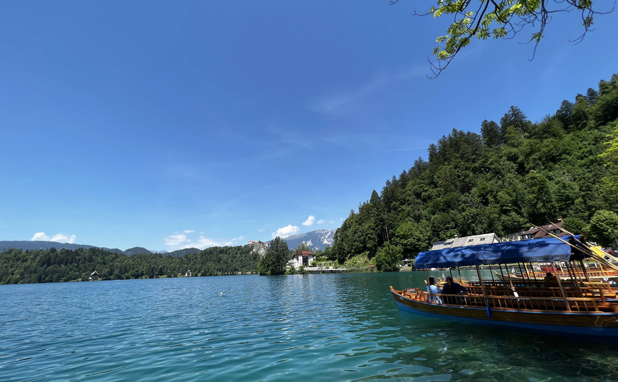 Boot auf klarem See vor bewaldeten Hügeln bei sonnigem Himmel