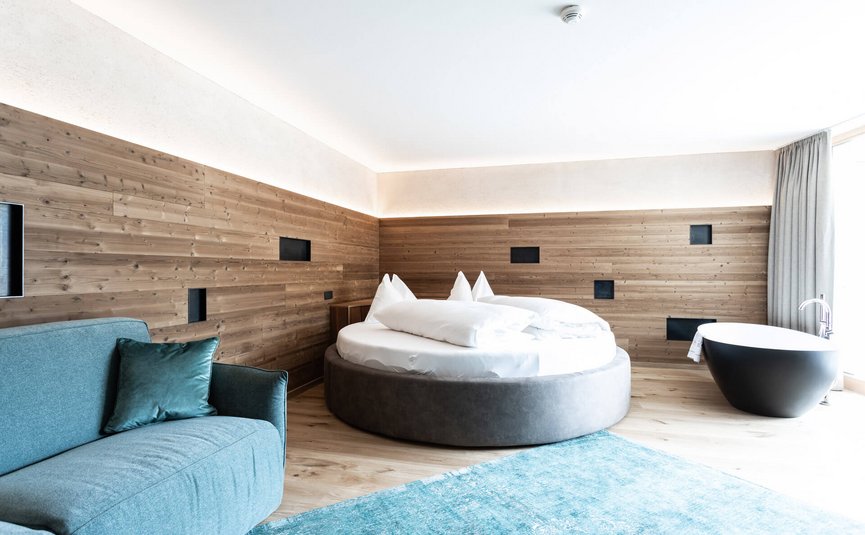 Motorrad- & Spa Hotel Traube Post am Reschensee **** © Theiner Karl-Heinz & Co KG Modernes Hotelzimmer mit Rundbett, blauer Couch und freistehender Badewanne