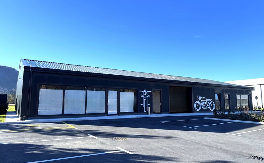 Hotel Grof **** © Hotel Grof Archive Schwarzes Gebäude mit Motorradsymbolen und leerem Parkplatz bei blauem Himmel