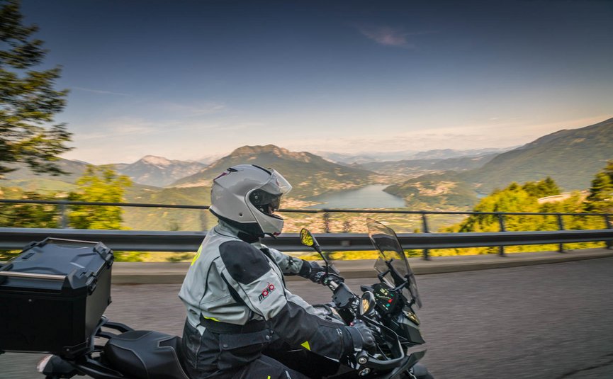 Motorradfahrer auf Bergstraße mit Blick auf See und Berge