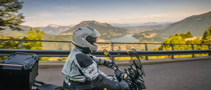 Motorradfahrer auf Bergstraße mit Blick auf See und Berge