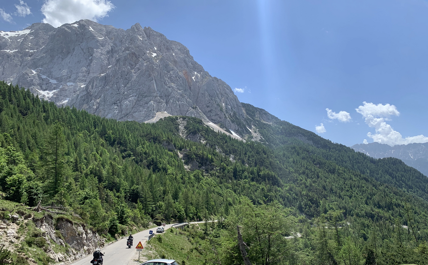 Bergstraße mit Fahrzeugen und Motorrädern unter blauem Himmel