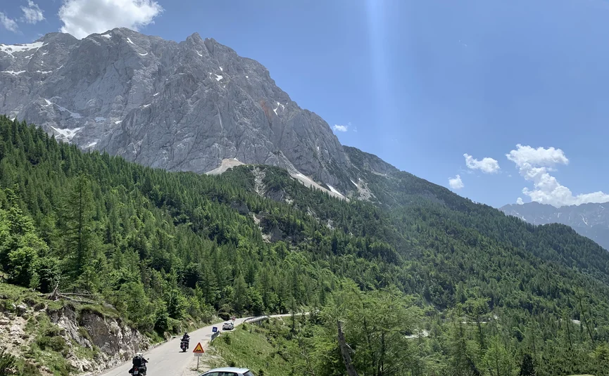 Bergstraße mit Fahrzeugen und Motorrädern unter blauem Himmel