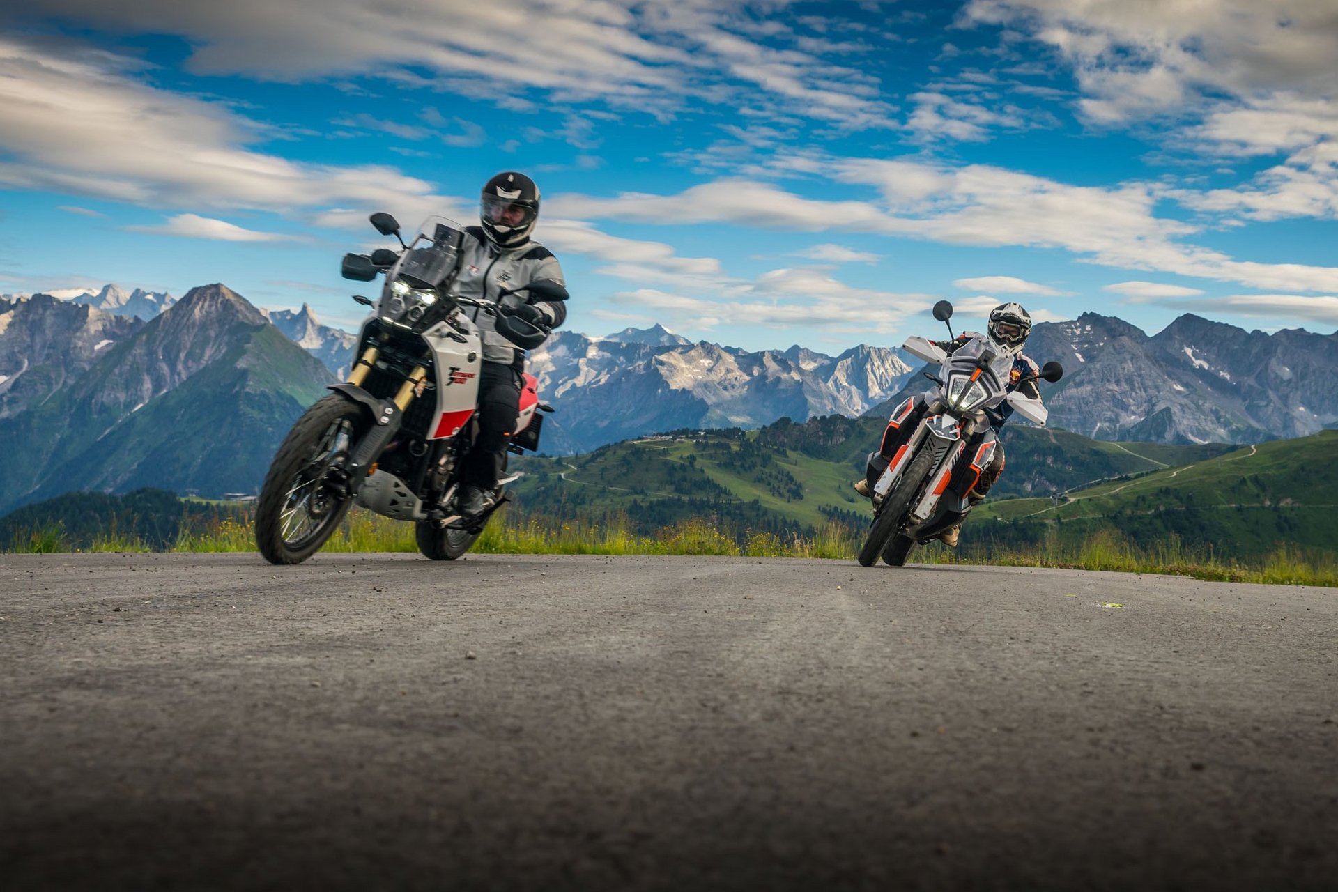 Zwei Motorradfahrer fahren auf einer Bergstraße mit Alpen im Hintergrund
