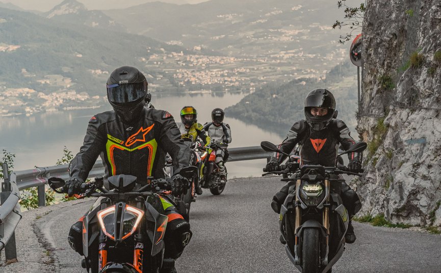 Vier Motorradfahrer fahren auf bergiger Straße mit Seeblick