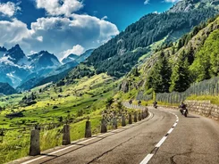 Motorradfahrer auf kurviger Bergstraße mit Alpenpanorama