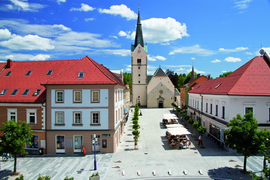 Stadtplatz mit Kirche und roten Dächern unter blauem Himmel