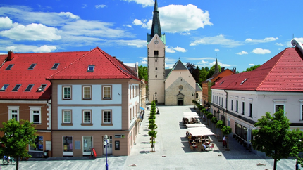Stadtplatz mit Kirche und roten Dächern unter blauem Himmel