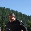 Karl Heinz Theiner © Theiner Karl-Heinz & Co KG Mann steht neben weiß-blauer BMW HP2 Motorrad in sonniger Berglandschaft