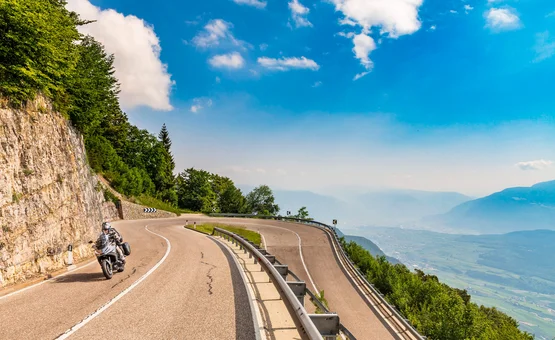 Motorcyclist on winding mountain road overlooking valley under clear sky