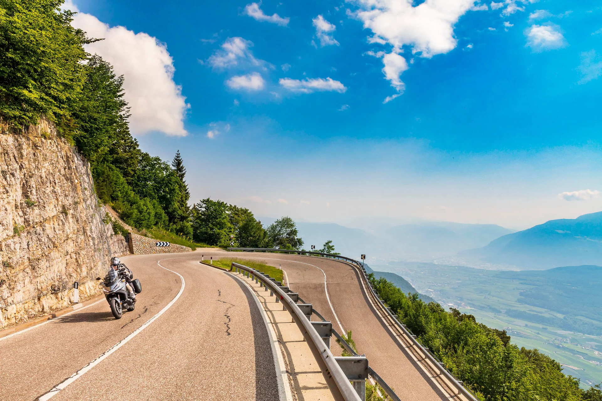 Motorcyclist on winding mountain road overlooking valley under clear sky