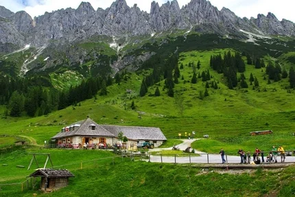 Mountain landscape with green valley and cabin beneath rocky peaks