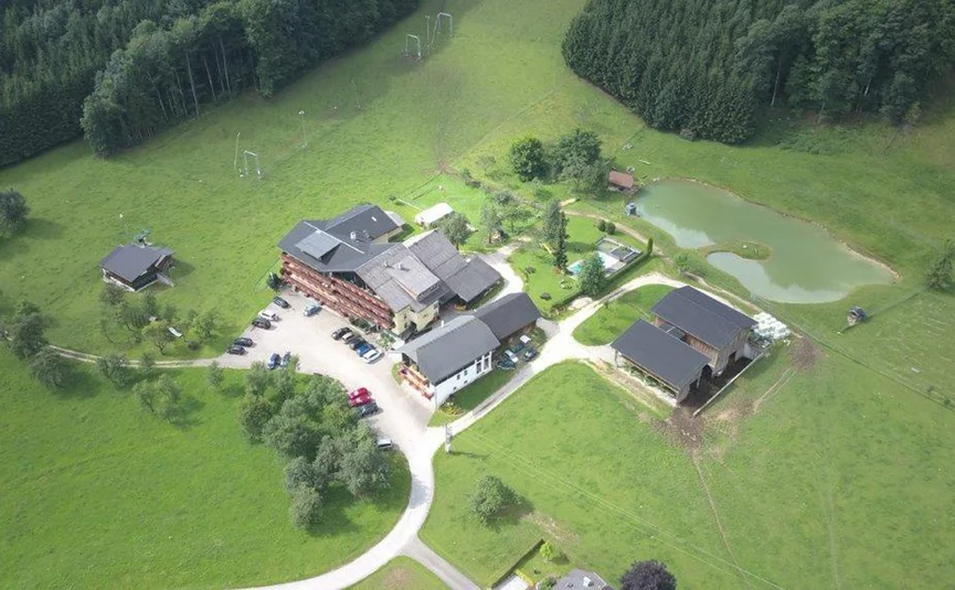 Aerial view of a small farm with buildings, pond, and green fields