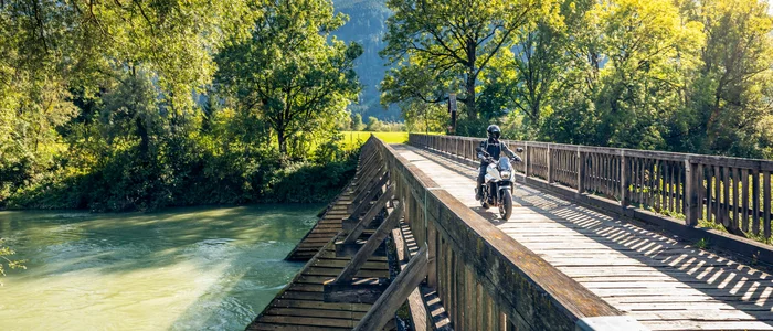 Motorradfahrer fährt über eine hölzerne Brücke bei sonnigem Wetter