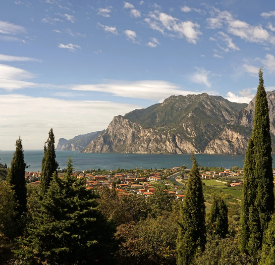 Blick auf einen See mit Bergen und Zypressen im Vordergrund