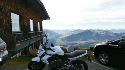 Kitzbüheler Horn Tour (Tour 7) Weiße Motorrad, Autos neben Holzhütte mit Bergpanorama im Hintergrund
