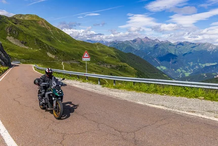 Motorcyclist on mountain road with green hills and distant peaks