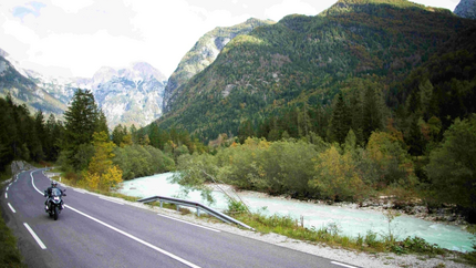 Motorcoureur op kronkelende weg langs rivier en bergen