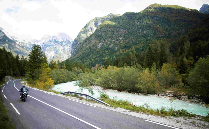 Emerald Soča River & Alpine Peaks Tour Motorcycle rider on winding road beside river and mountains