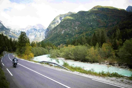 Motorcycle rider on winding road beside river and mountains