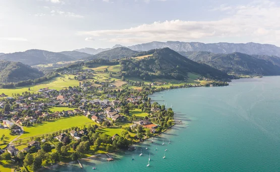 Luftaufnahme eines Sees mit Dorf und Bergen im Hintergrund