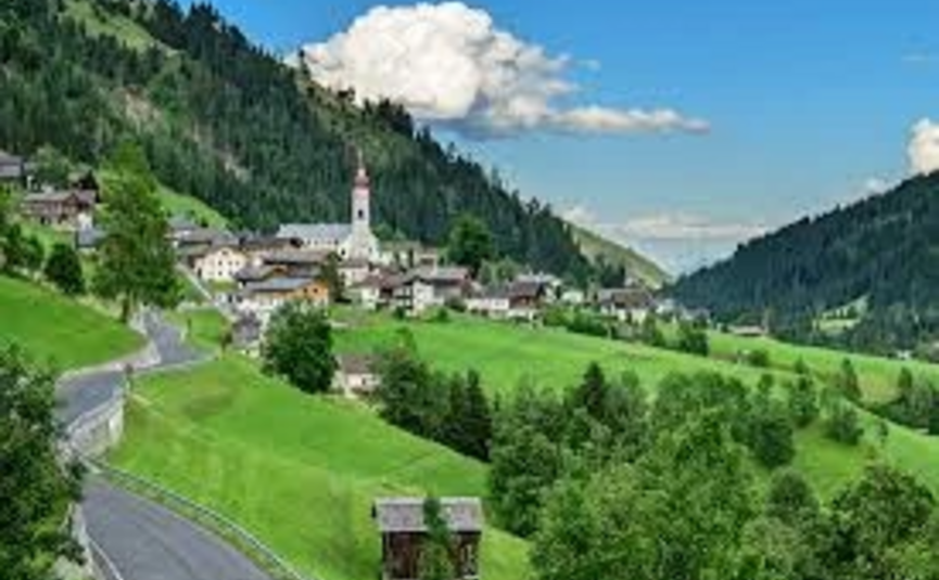 Dorf im grünen Tal mit Kirche und Bergen unter blauem Himmel