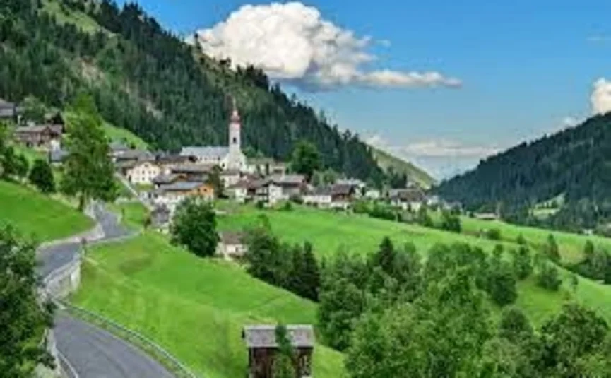 Dorf im grünen Tal mit Kirche und Bergen unter blauem Himmel