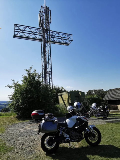 Motorcycles in front of a large metal cross on a hill