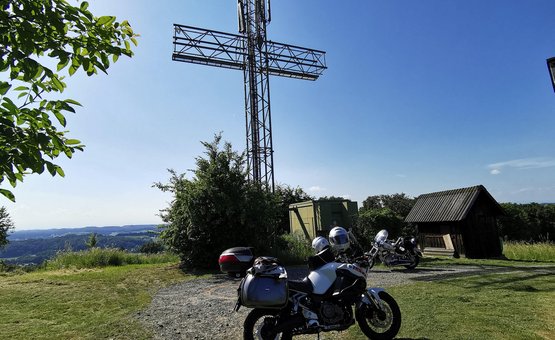 Motorräder vor einem großen metallischen Kreuz auf einem Hügel