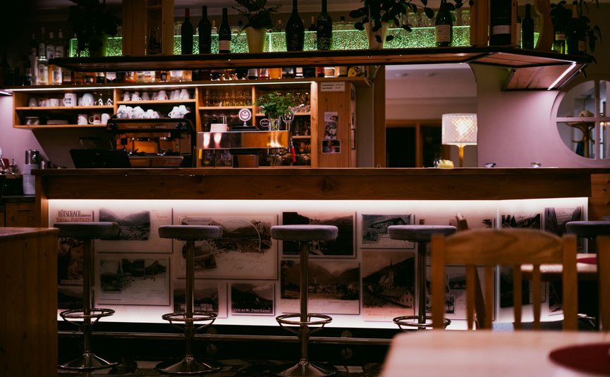 Gemütliche Bar mit beleuchteter Holztheke und hohen Barhockern