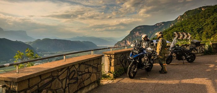 Zwei Motorradfahrer in Ausrüstung mit Motorrädern auf Bergstraße bei Sonnenuntergang