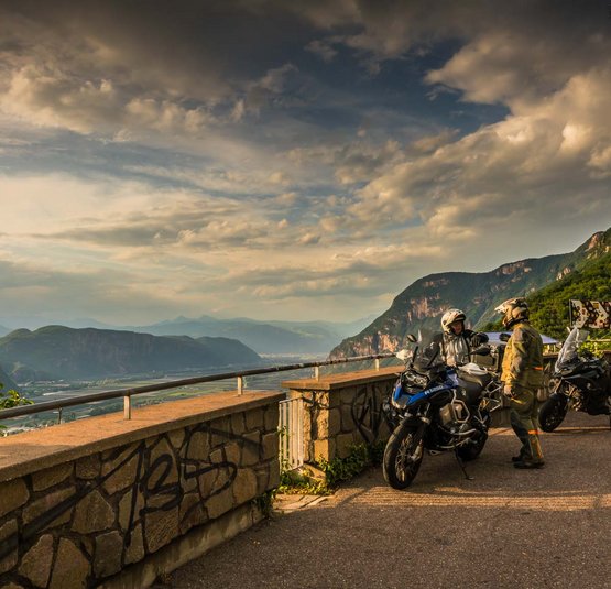 Zwei Motorradfahrer in Ausrüstung mit Motorrädern auf Bergstraße bei Sonnenuntergang