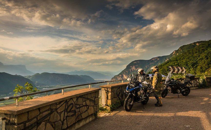 Zwei Motorradfahrer in Ausrüstung mit Motorrädern auf Bergstraße bei Sonnenuntergang