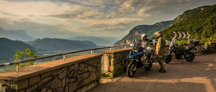 Zwei Motorradfahrer in Ausrüstung mit Motorrädern auf Bergstraße bei Sonnenuntergang