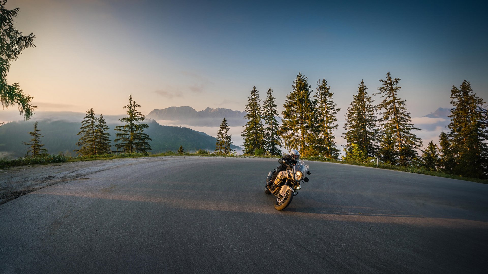 Motorradfahrer auf kurviger Bergstraße bei Sonnenuntergang