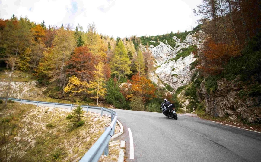 Motorradfahrer auf kurviger Bergstraße im herbstlichen Wald