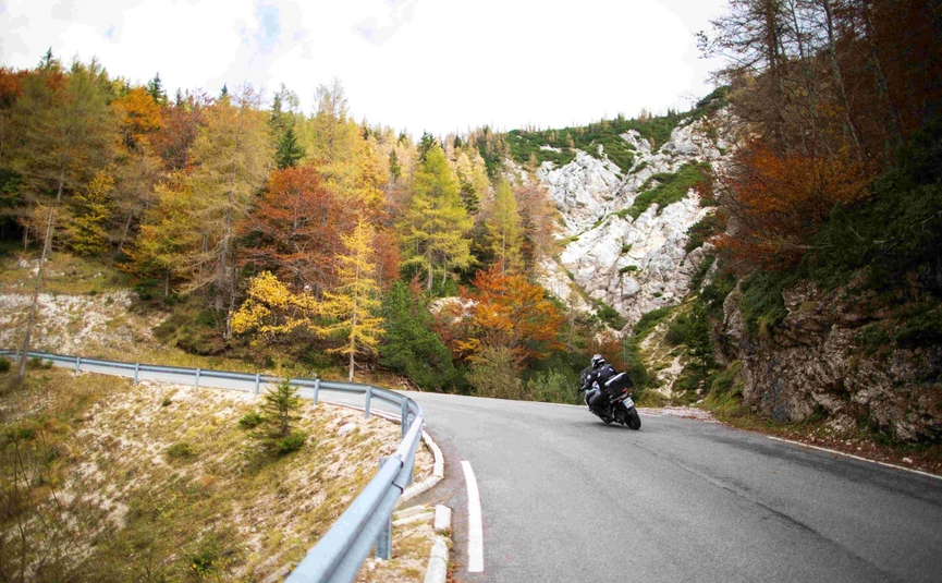 Emerald Soča River & Alpine Peaks Tour Motorcyclist on winding mountain road in autumn forest