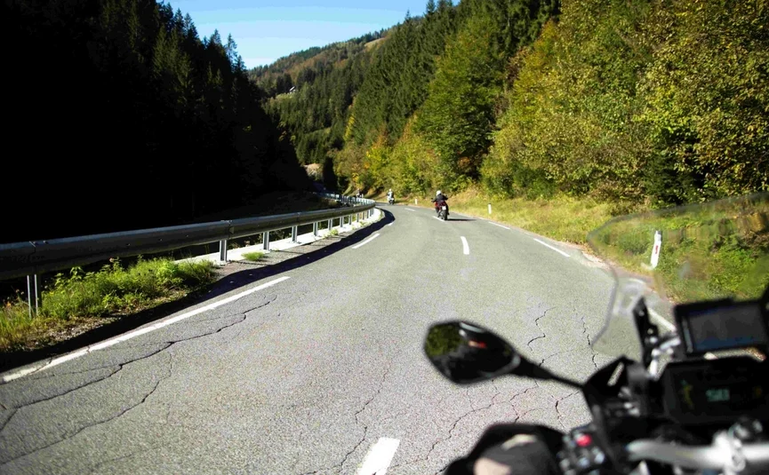 The Carinthia Heritage Ride Blick von Motorradfahrers Perspektive auf kurvige Straße durch bewaldete Berge