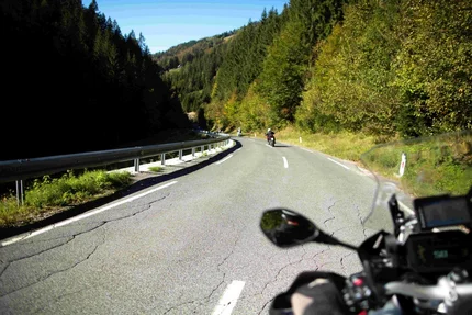 View from motorcyclist perspective on winding road through forested mountains