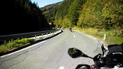 Zicht vanuit motorfietsrijder op kronkelende weg door beboste bergen